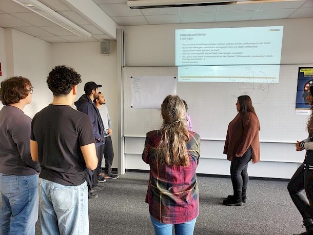 Gruppe von Studierenden vor einer Leinwand mit AGFS-Präsentation zu Leitfragen der Stadt- und Mobilitätsplanung